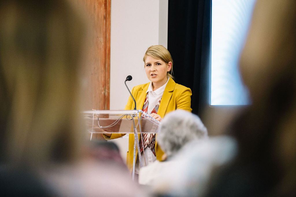 A photograph of a woman at a lectern. LaurynOates, taken on 2019-05-02 at Changemakers by Connie Tsang.
